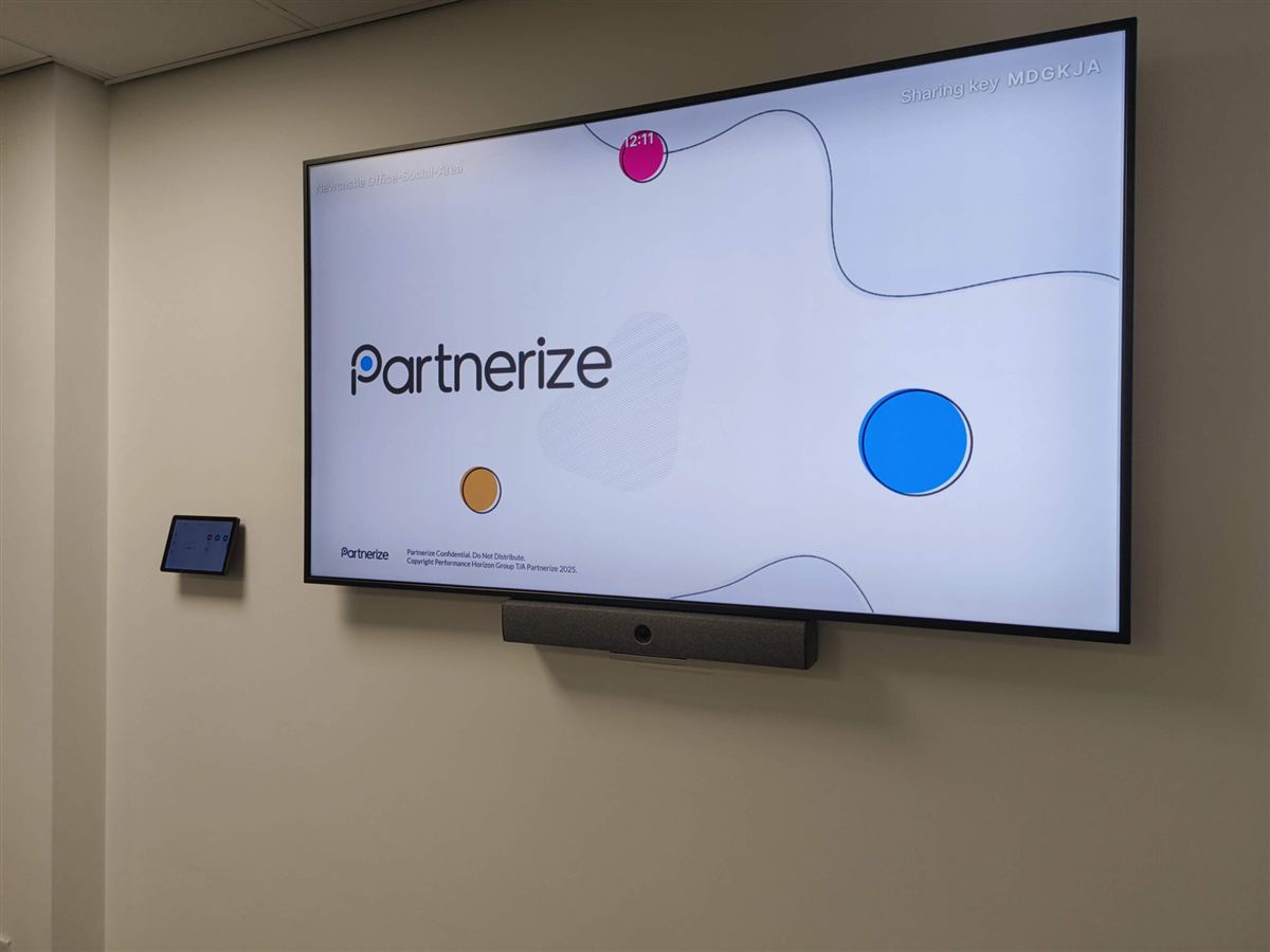 Large meeting room display with video conferencing bar and room booking panel in the Partnerize Newcastle office