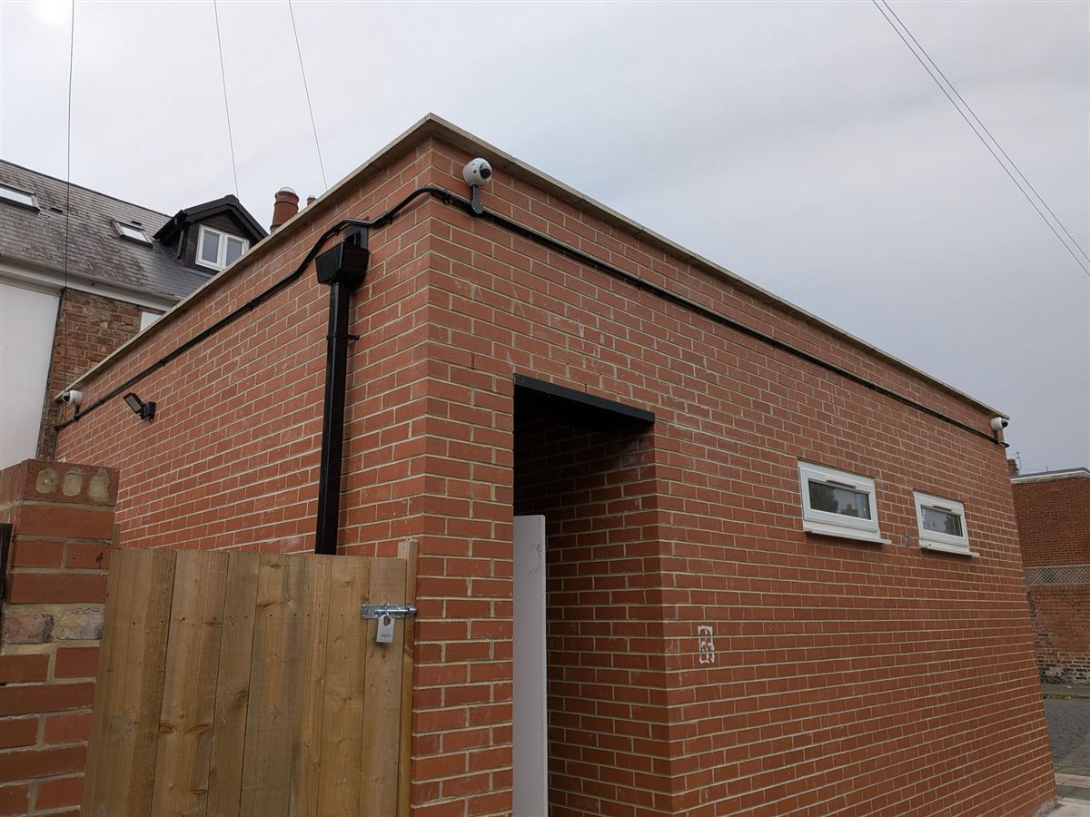 Three CCTV cameras and neat cable runs on a brick building beside a back lane in Wallsend
