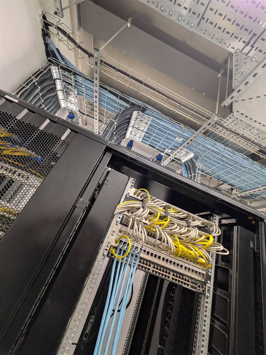 Network rack with patch panels and switches, fed by data cabling on overhead cable tray