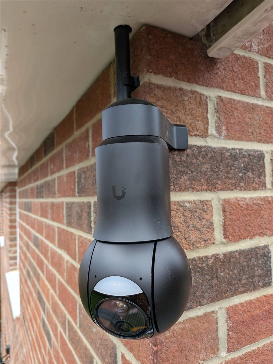 UniFi Protect PTZ camera mounted on a brick wall under the eaves